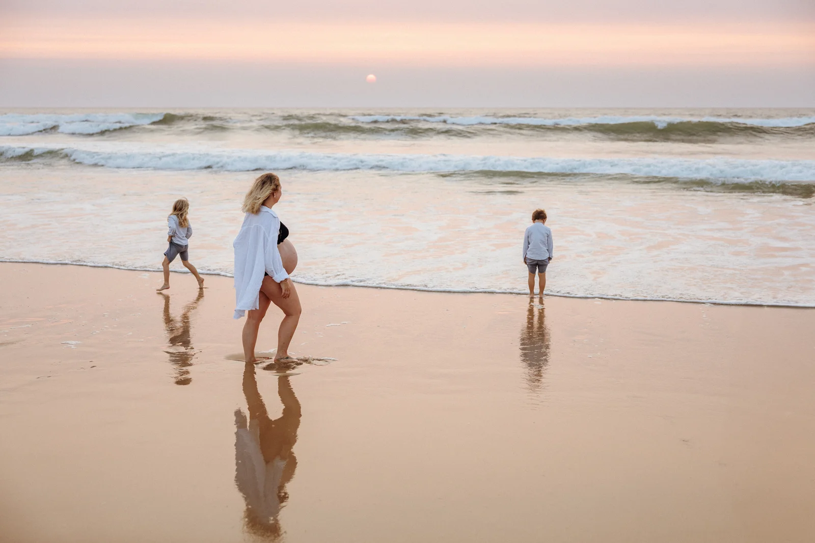 Maman enceinte sur une plage des Landes au coucher du soleil avec deux enfants jouant au bord de l’océan