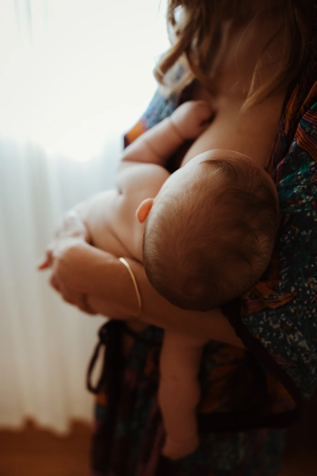 Maman portant son bébé après une tétée pendant une séance photo allaitement à domicile