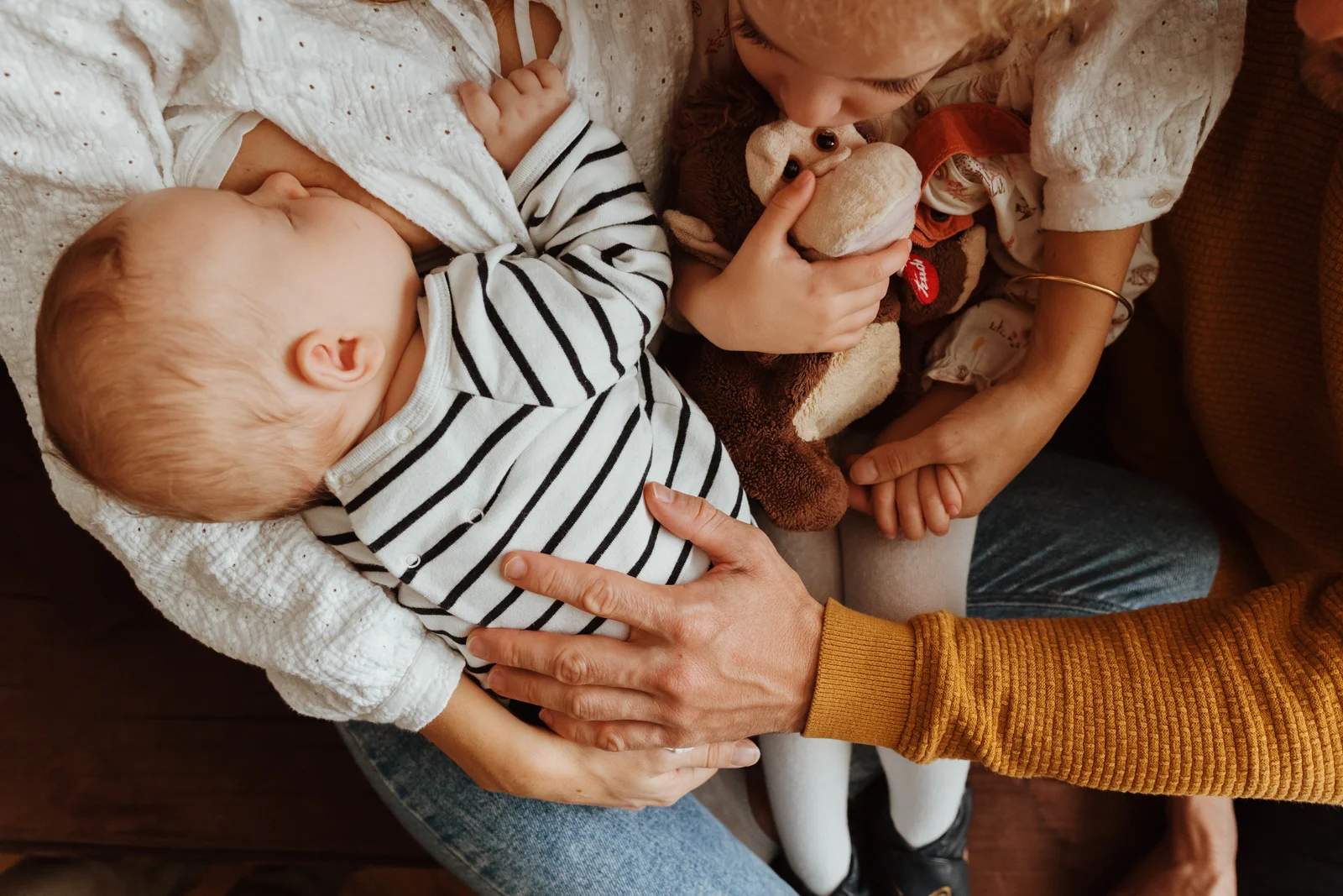 Détail des bras d’une famille autour de leur bébé pendant une séance photo à domicile