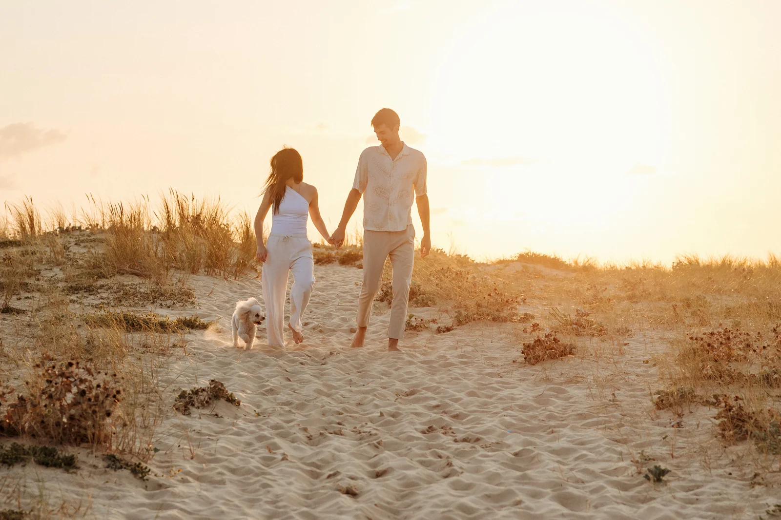 Couple marchant dans les dunes avec leur chien au coucher du soleil