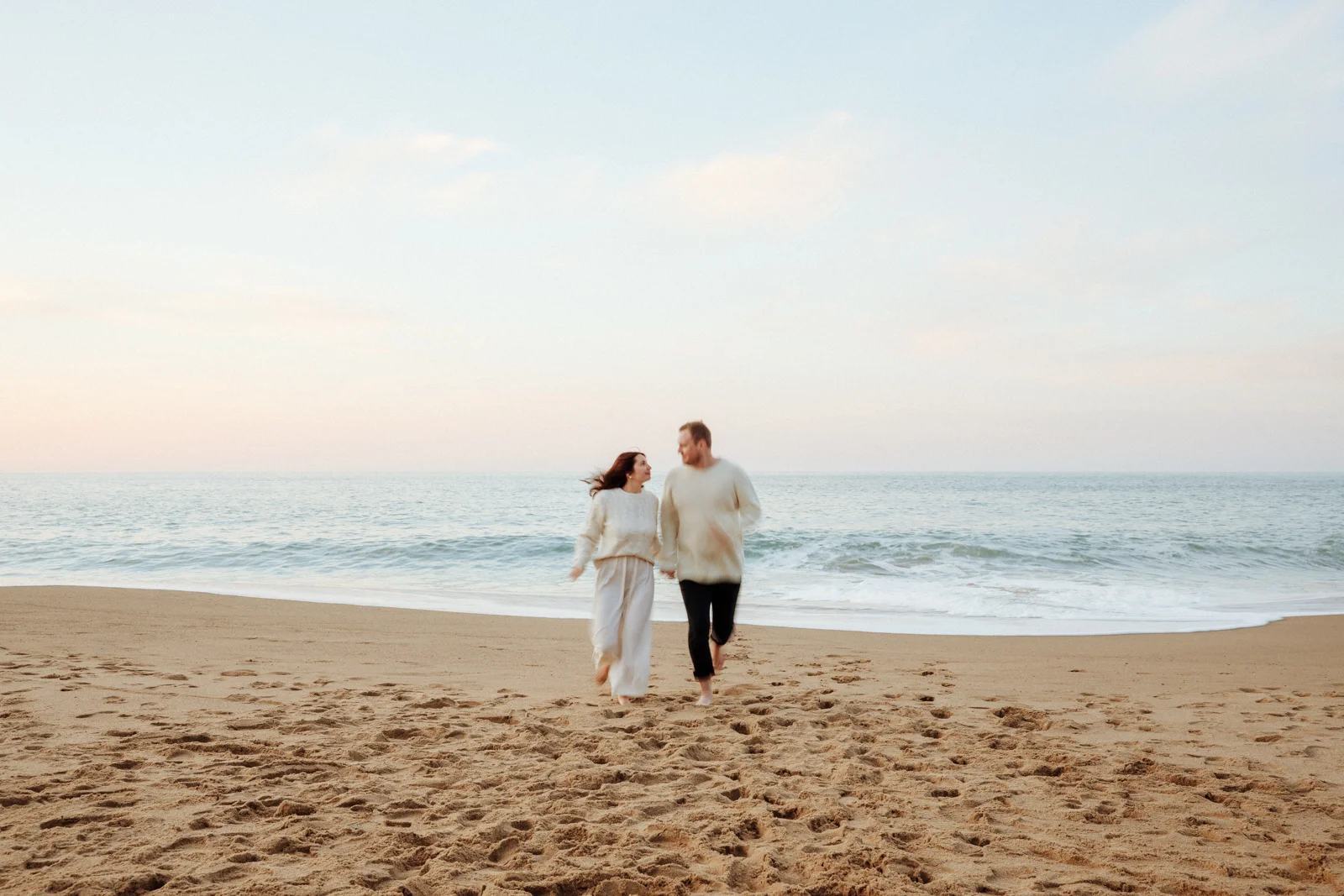 couple courant sur la plage face à l’océan lors d’une séance photo en vacances dans les Landes