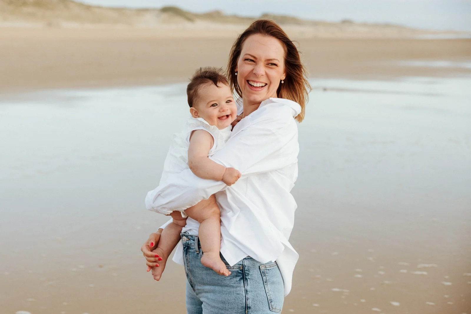 maman souriante avec son bébé dans les bras lors d’une séance photo famille sur la plage dans les Landes