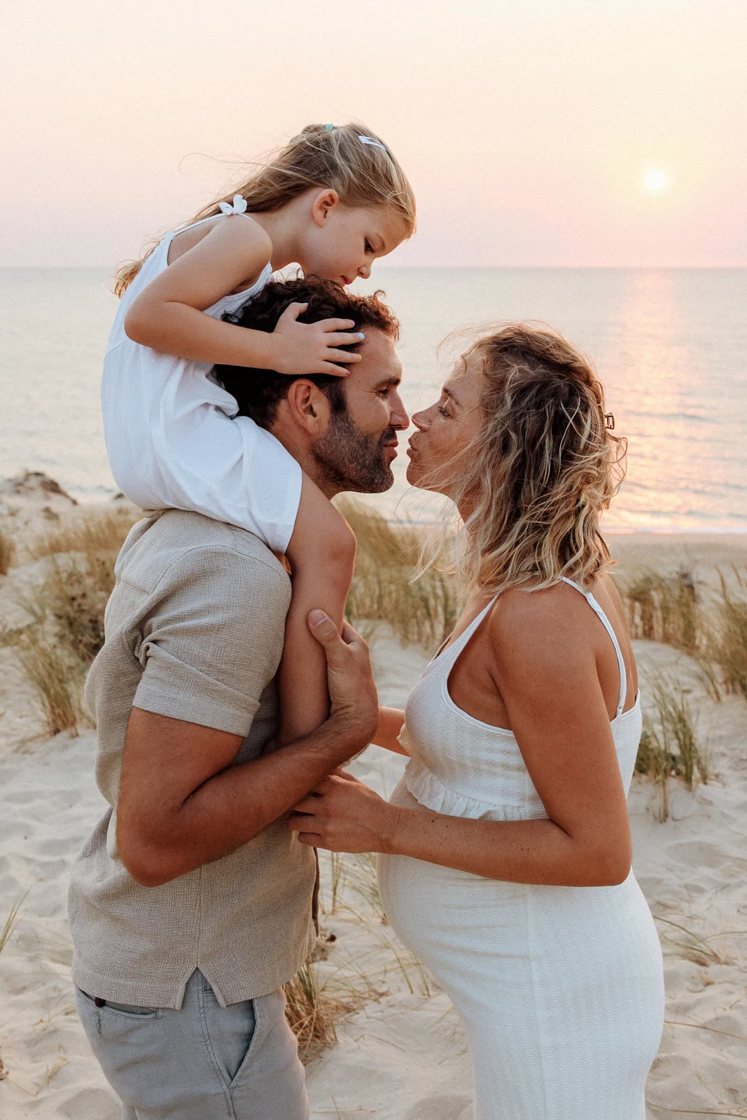 parents avec leur enfant au coucher du soleil face à l’océan lors d’une séance photo dans les Landes