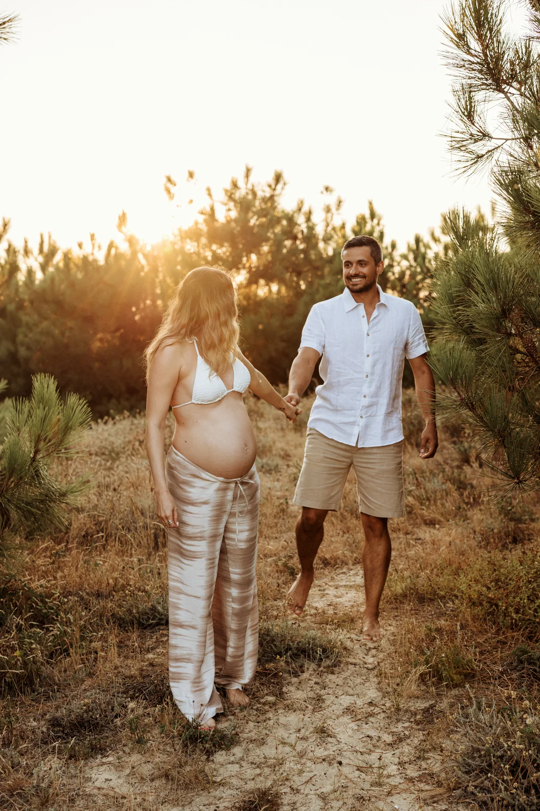 couple avec femme enceinte marchant dans la forêt au coucher du soleil lors d’une séance photo dans les Landes