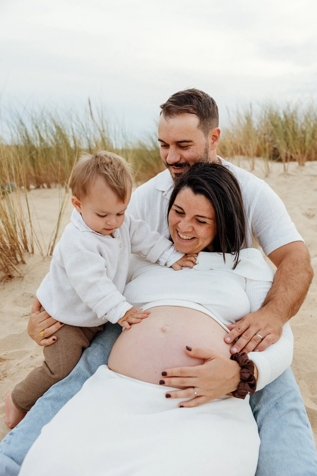 femme enceinte avec son conjoint et leur enfant dans les dunes lors d’une séance photo en vacances dans les Landes