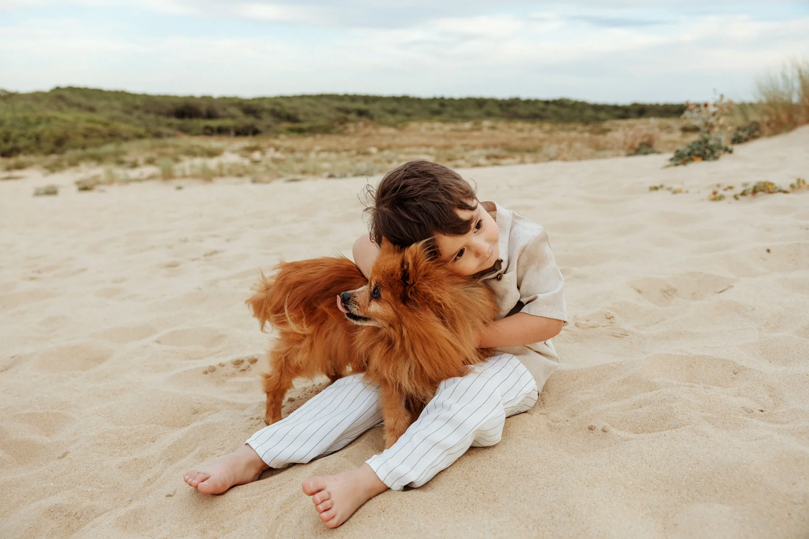 Enfant assis dans le sable avec un petit chien lors d’une séance photo famille sur la plage dans les Landes