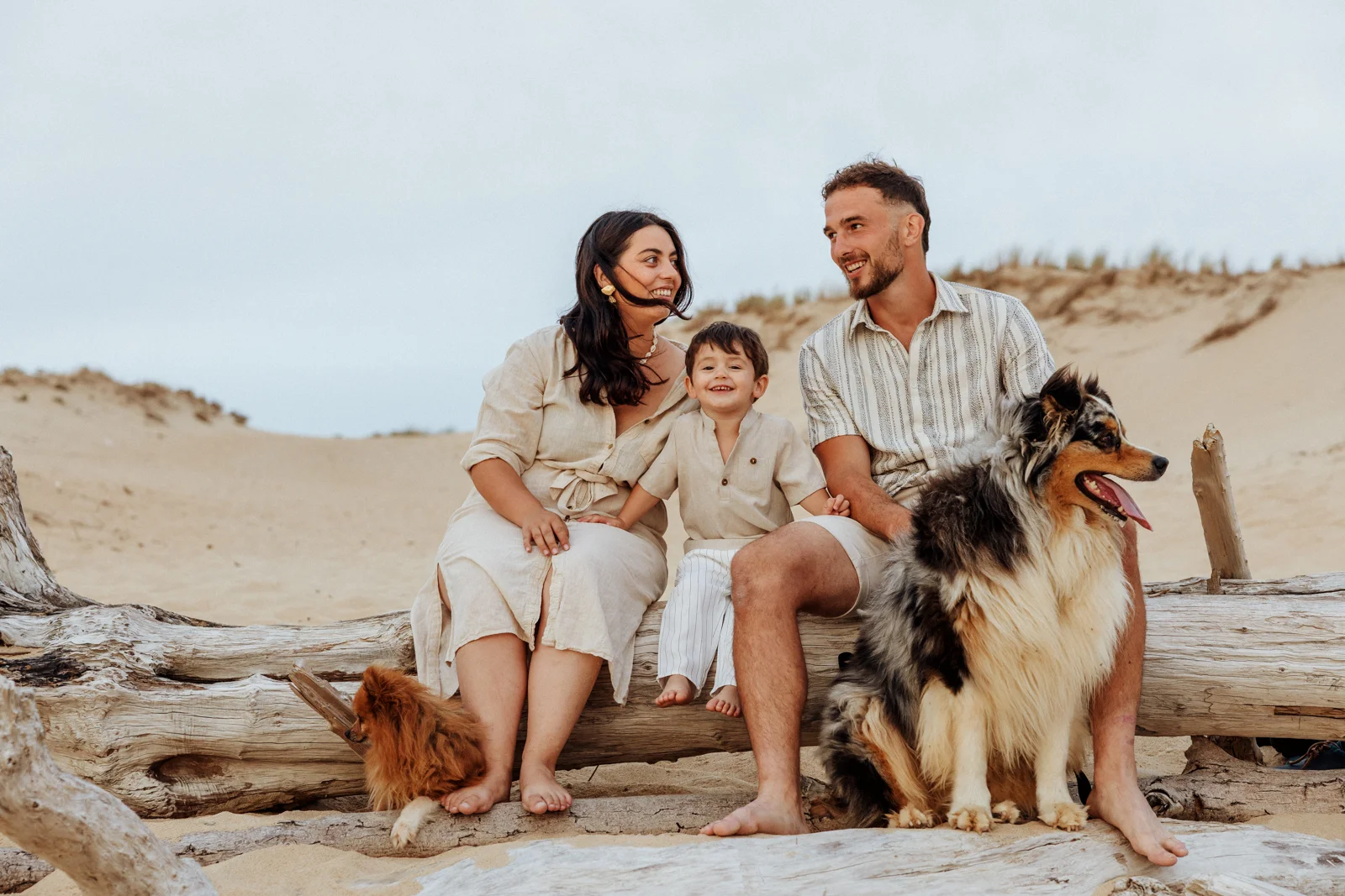 Famille assise sur du bois flotté avec leurs deux chiens pendant une séance photo sur la plage de Soustons dans les Landes