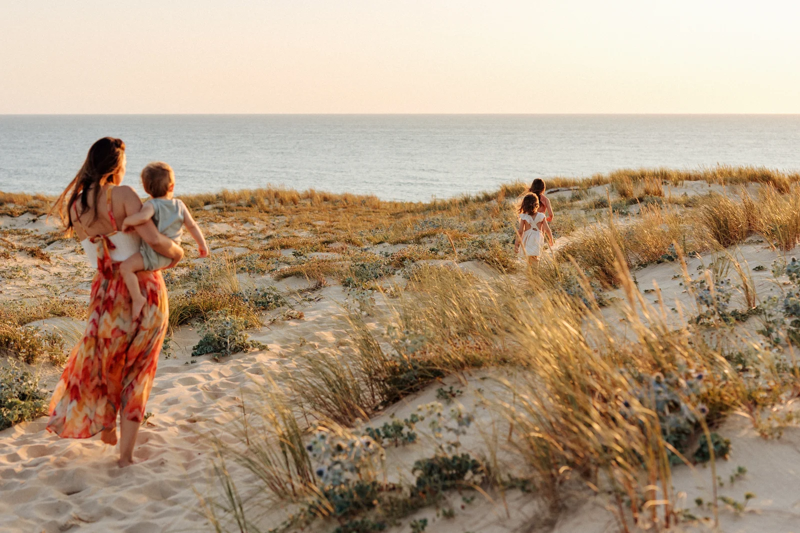 Maman avec ses enfants dans les dunes face à l’océan au coucher du soleil pendant une séance photo dans les Landes