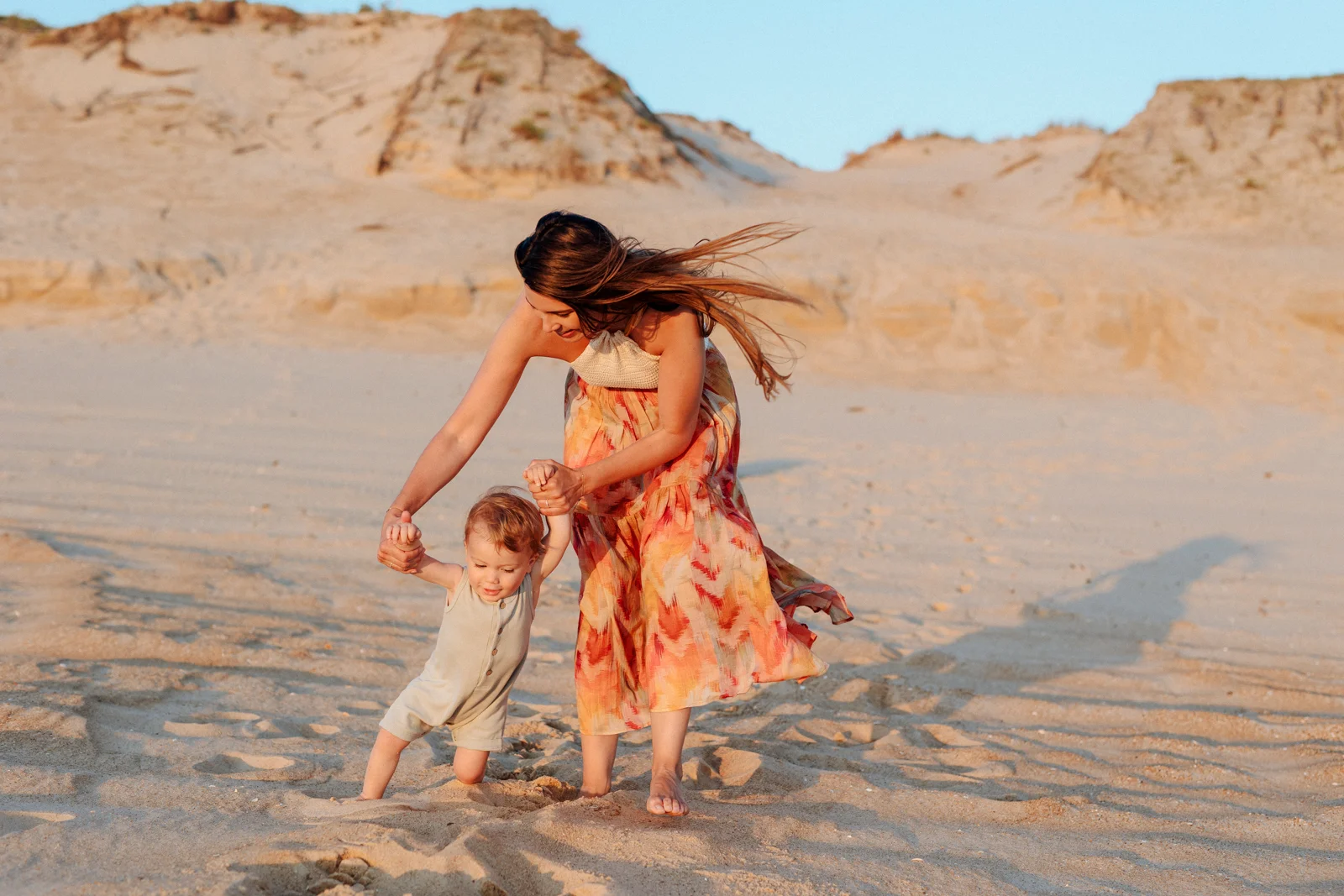Maman tenant les mains de son enfant sur la plage en fin de journée pendant une séance photo dans les Landes
