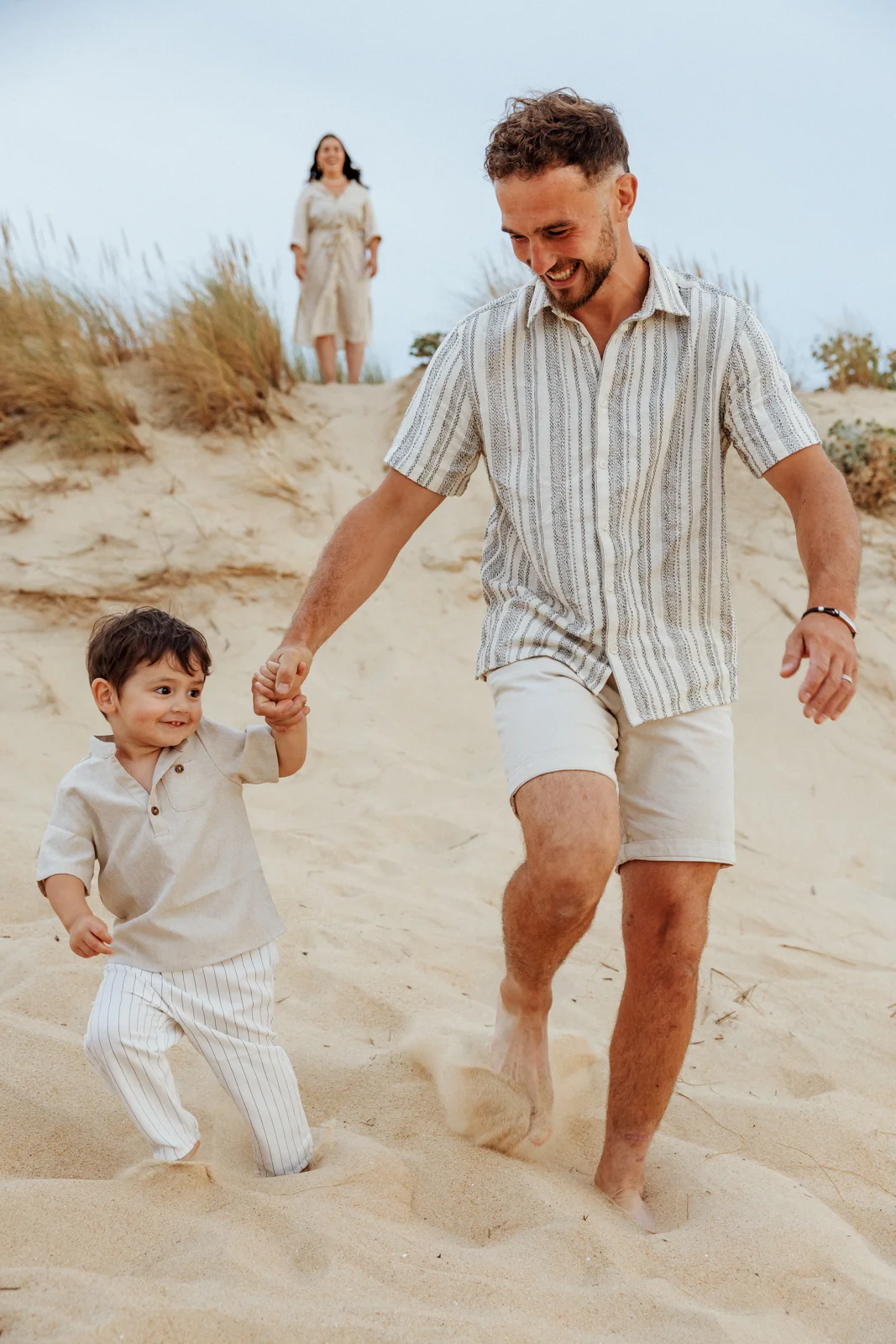 Papa tenant la main de son fils dans les dunes pendant une séance photo famille à Soustons dans les Landes