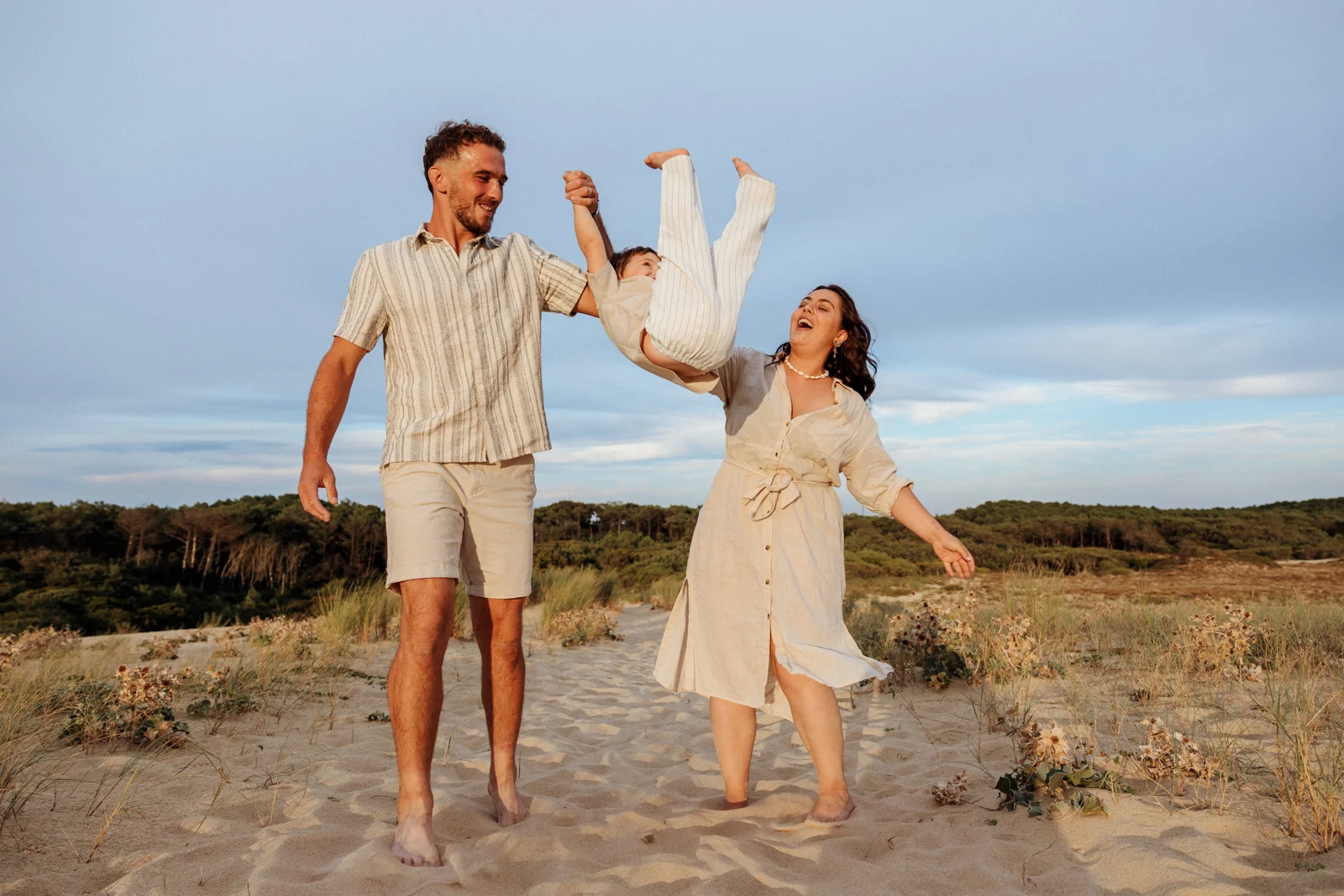 Parents faisant tourner leur enfant pendant une séance photo famille sur la plage dans les Landes