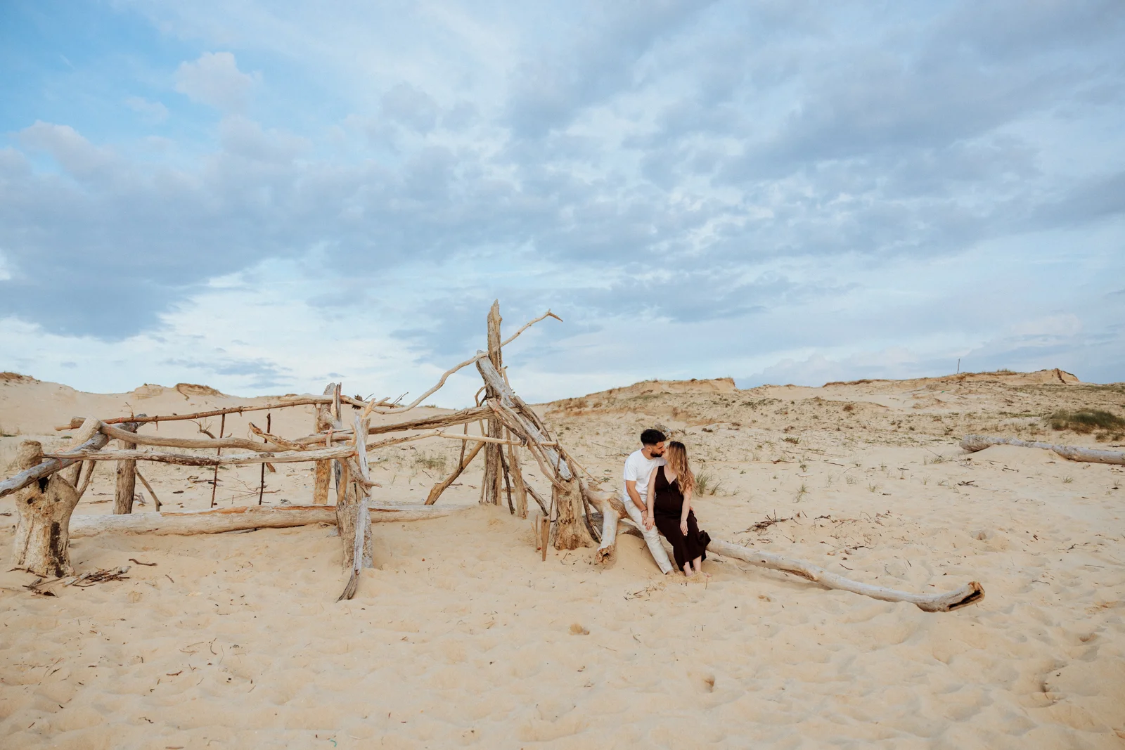 Couple assis sur une plage sauvage des Landes au coucher du soleil pendant une séance photo grossesse lifestyle