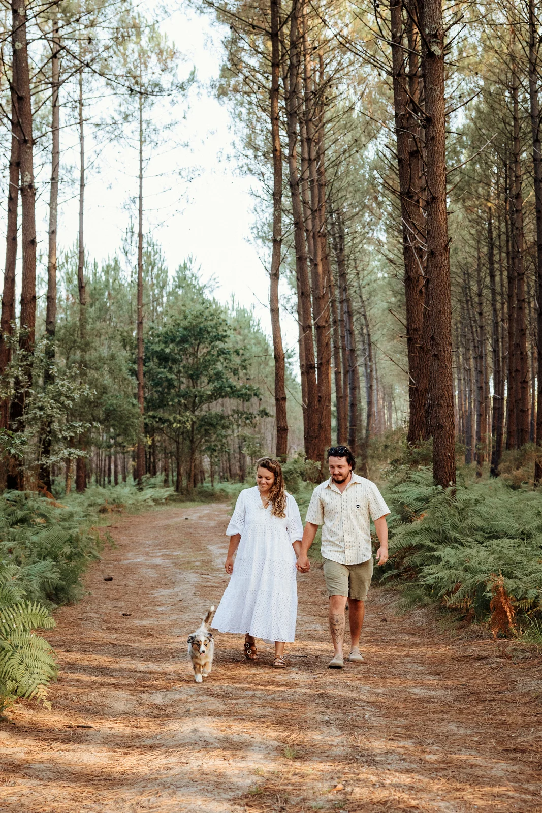 Couple se promenant avec son chiot berger américain dans la forêt landaise
