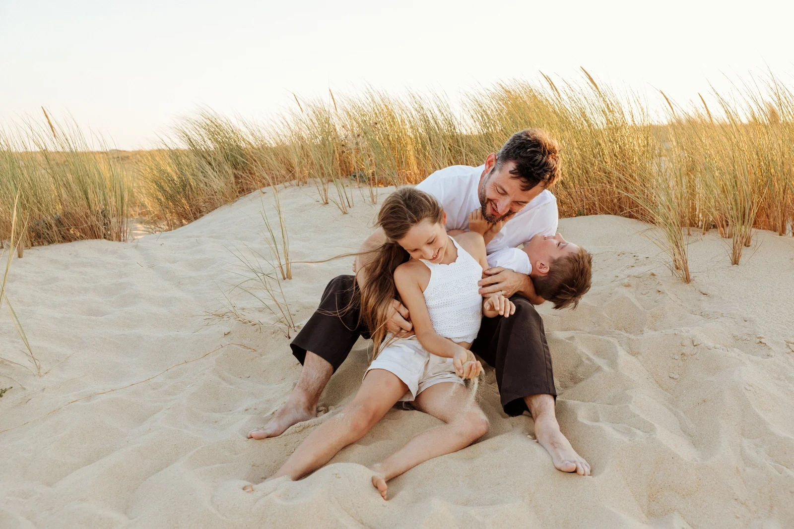Famille assise dans les dunes au coucher du soleil lors d'une séance photo de vacances dans les Landes