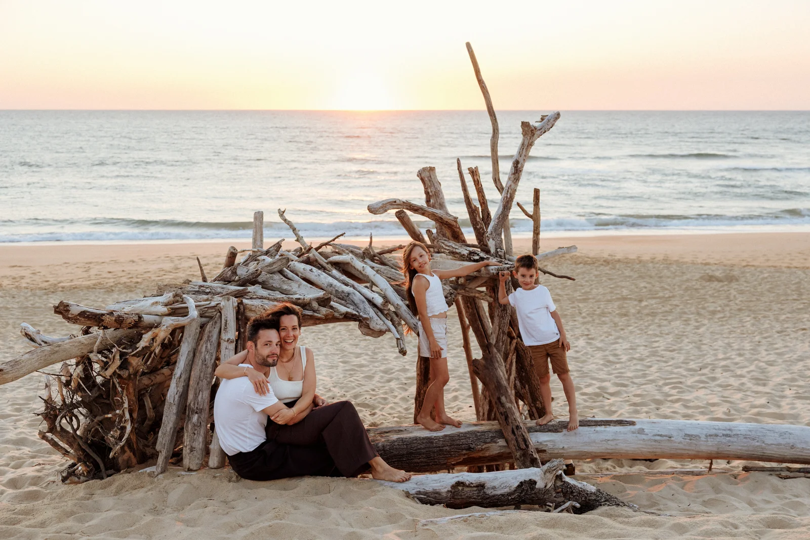 Séance photo famille sur une plage des Landes devant une cabane en bois flotté au coucher du soleil