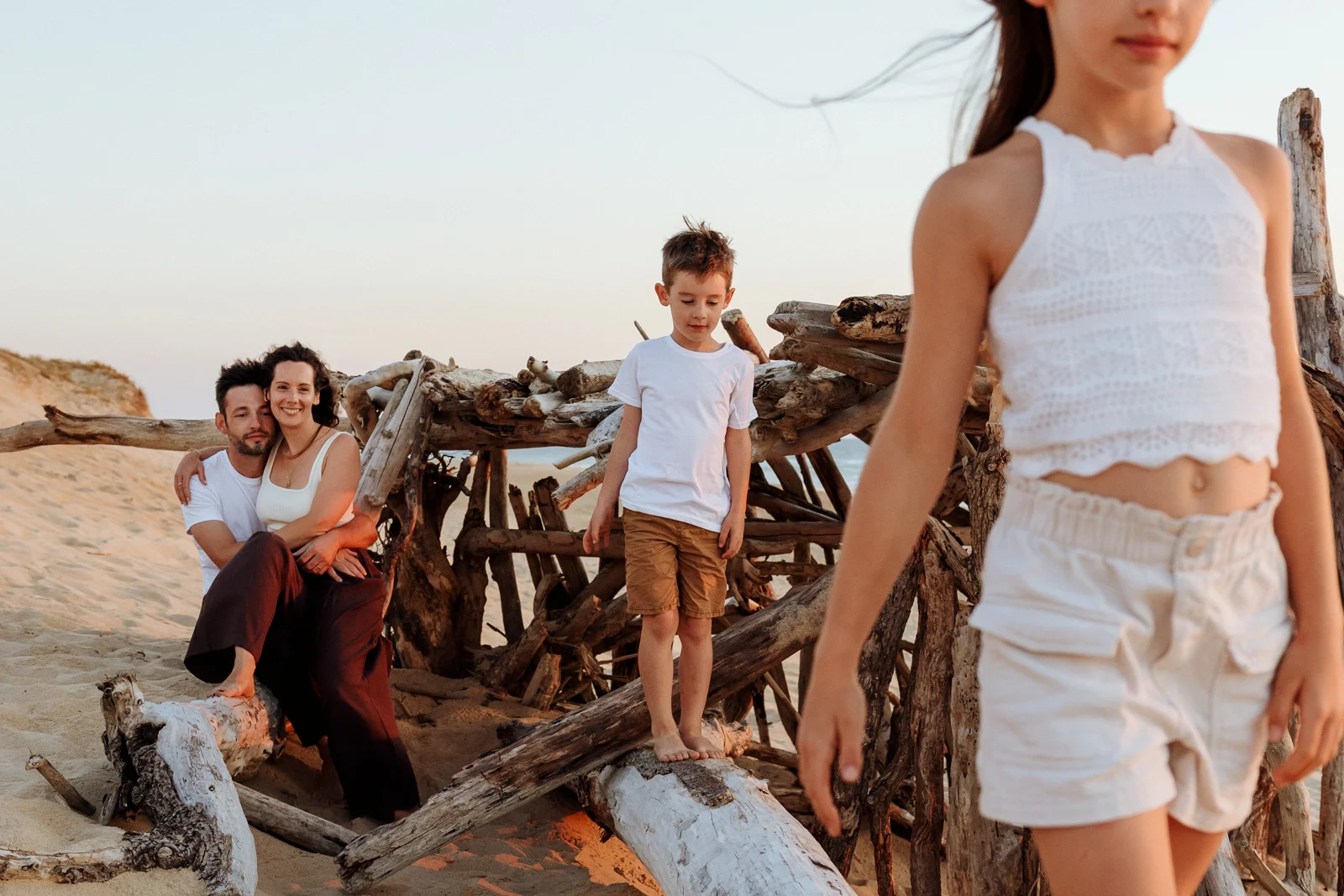 Enfants explorant une cabane en bois flotté sur une plage des Landes au coucher du soleil