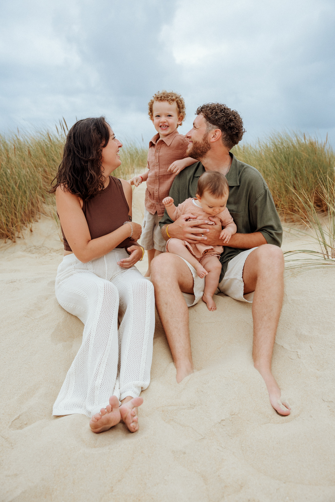 Une famille avec ses deux jeunes enfants réunie dans les dunes lors d'une séance photo famille sur une plage des Landes.